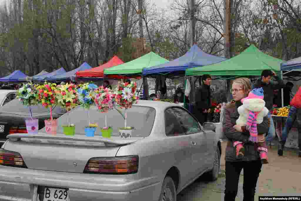 Рысқұлов көшесіндегі гүл базарында бала көтеріп тұрған әйел.